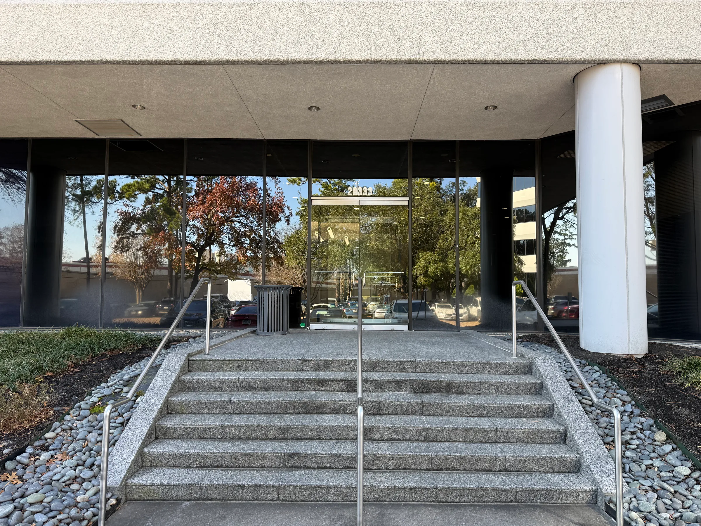 Modern office building entrance with glass doors, concrete steps, and metal railings.