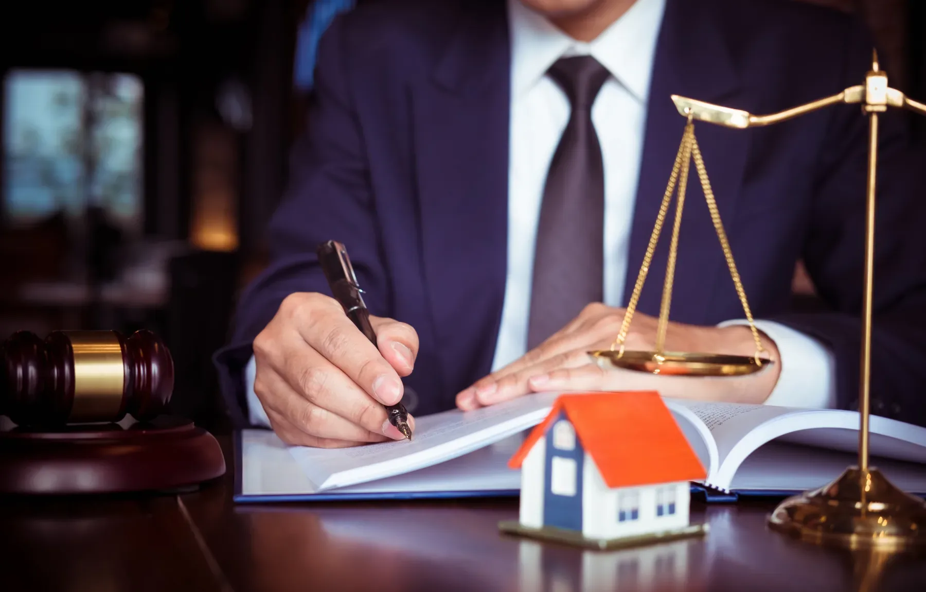 Real estate attorney reviewing property documents with scales of justice and model house on desk, symbolizing legal complianc